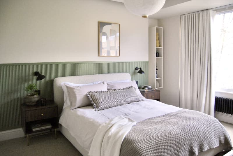 guest bedroom with green⁢ wainscoting,‍ white⁣ walls, bed with white and⁣ gray linens, neutral flatweave carpet, patterned gray area rug, white pendant⁢ lantern