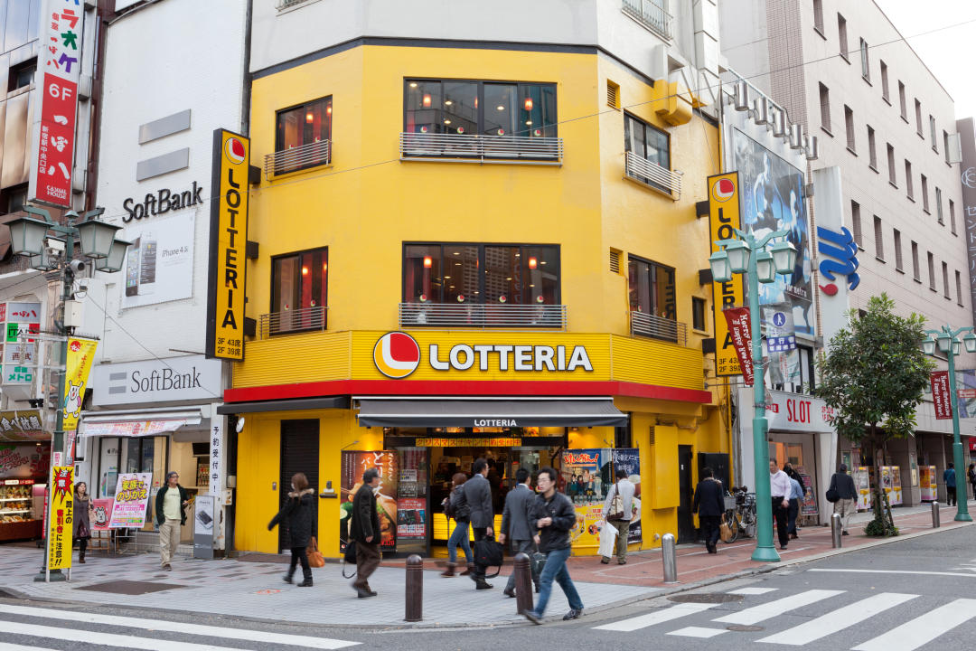 Pedestrians​ passing Lotteria⁢ restaurant chain advertisement.